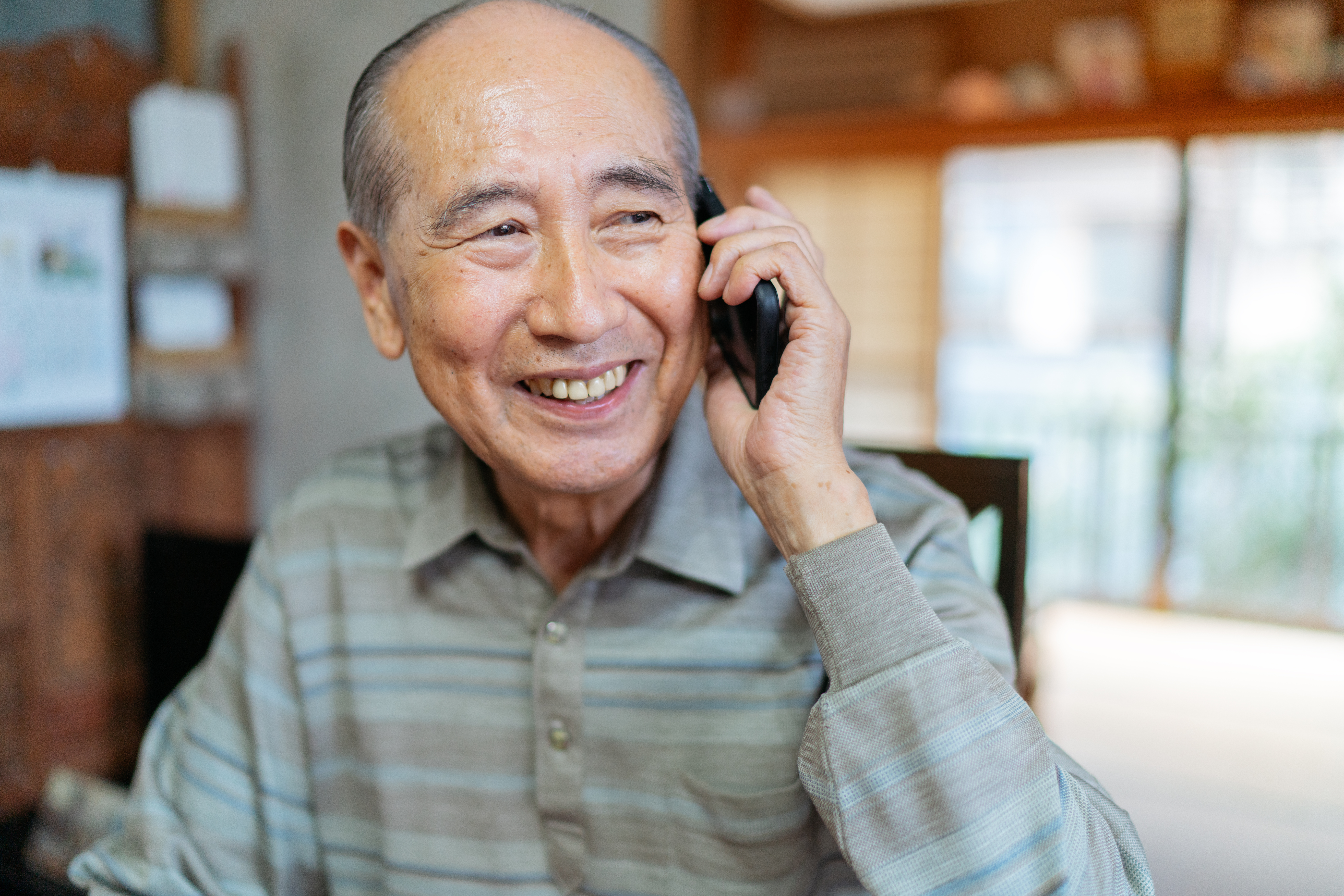 Older man is smiling as he talks on the phone
