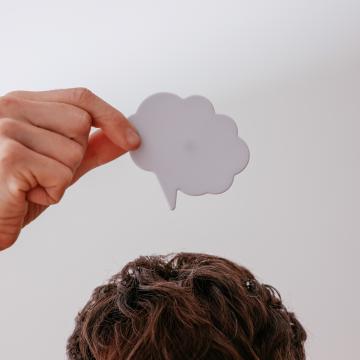 Person holding a paper cutout of a speech bubble above their head