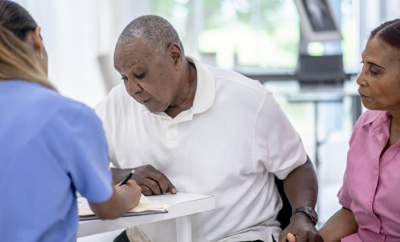 Elderly man looks at a piece of paper while holding his wife's hand