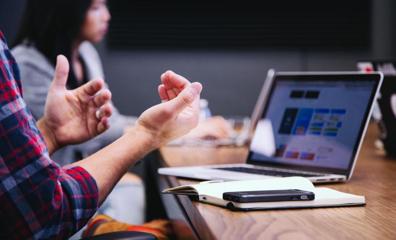 A stock photo showing someone talking at a meeting with a PC in front of them