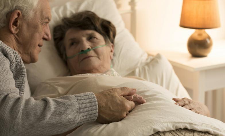 A woman in bed being cared for by her husband
