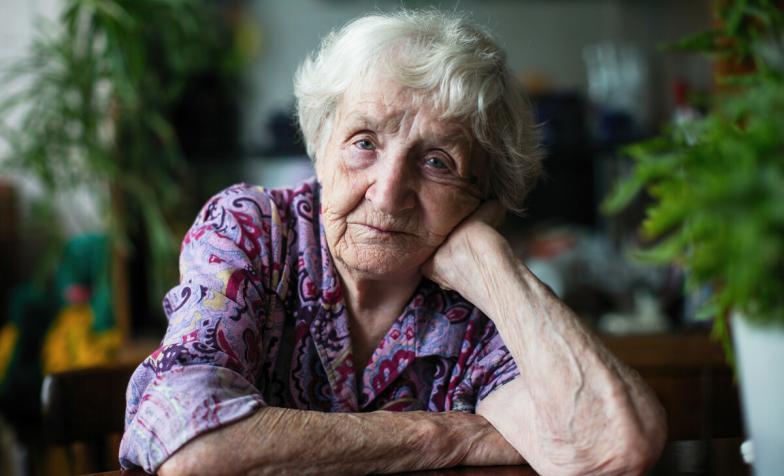 An older woman looks at the camera with plants in the background