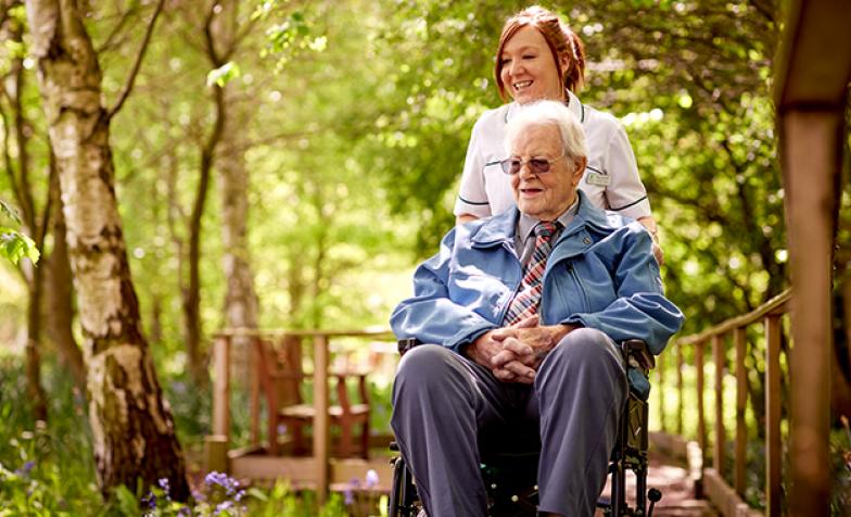A hospice nurse with a patient in a wheelchair admiring the hospice gardens