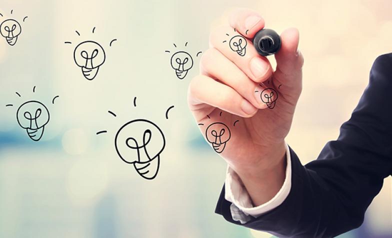 Stock photo of a hand, holding a pen, drawing lightbulbs on a transparent surface