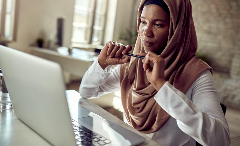 Woman wearing head scarf sitting at desk with laptop