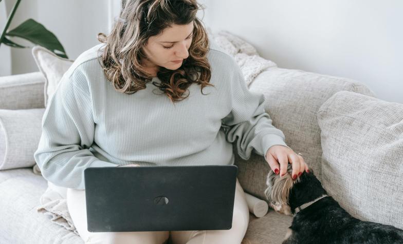 woman sitting on a couch with a pet dog and a laptop