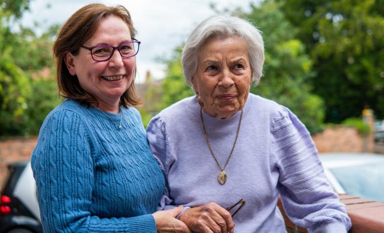One woman with dark hair supports another with white hair outside.