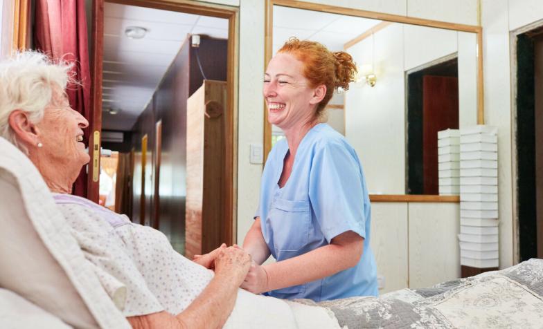 Laughing nurse sits at the bed of an elderly woman