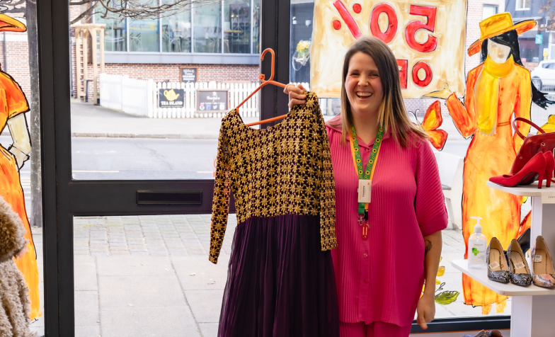 Woman standing in shop holding up dress on hanger
