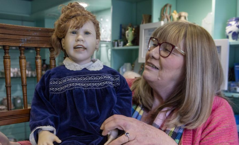 A lady with glasses holding a doll 
