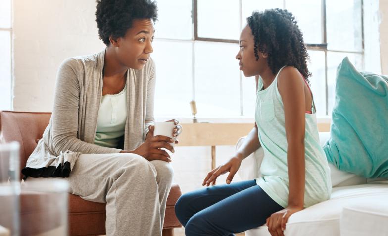 A mother holding a hot drink and sitting in conversation with a young girl