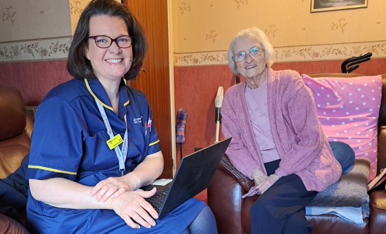 A elderly patient sat on an armchair next to a palliative care nurse