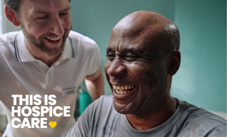 A man in a grey t shirt is laughing with a man in a white t shirt. The text in the corner reads 'This is hospice care'.