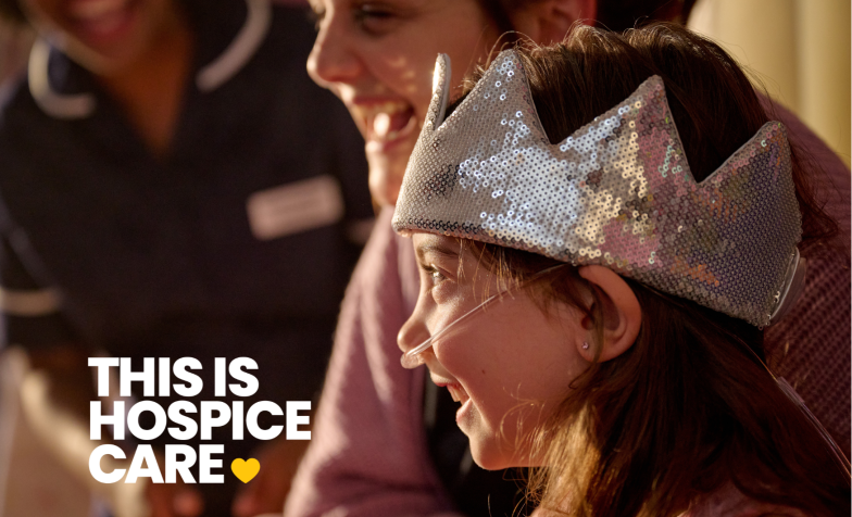A girl in a crown wearing an oxygen tube is laughing with her mum and a nurse. The text in the corner reads 'This is hospice care'.