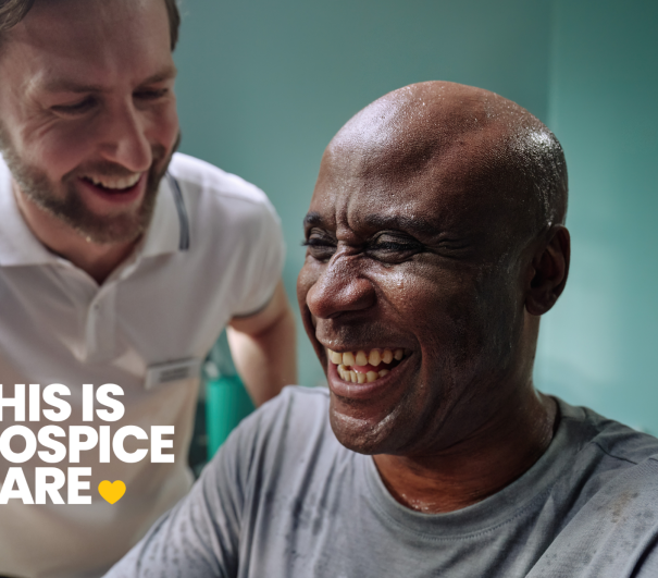 A man in a grey t shirt is laughing with a man in a white t shirt. The text in the corner reads 'This is hospice care'.