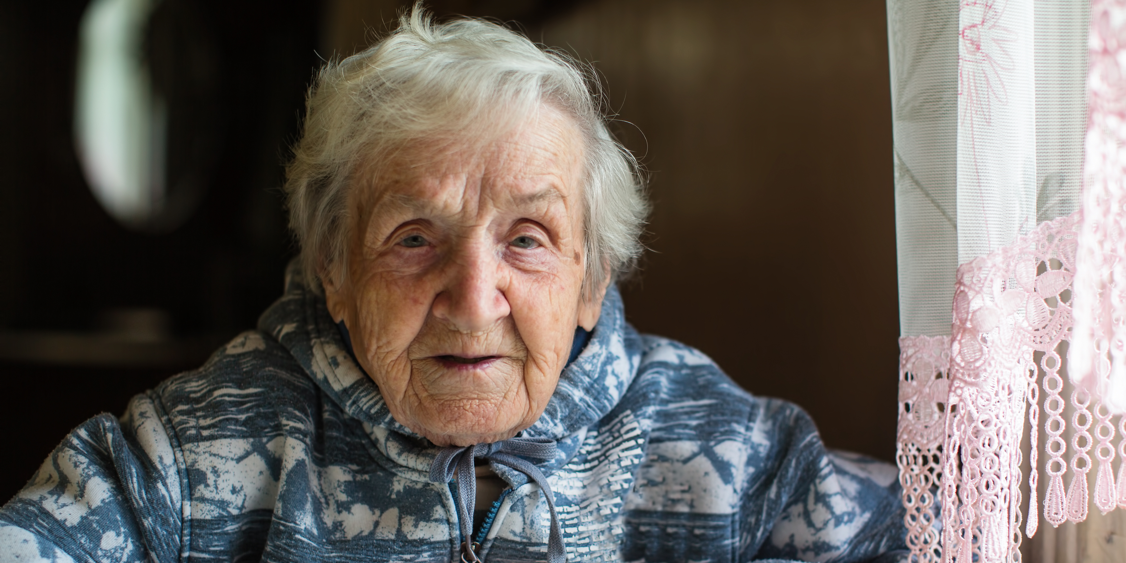 An elderly white lady with grey hair is looking calmly directly at the camera