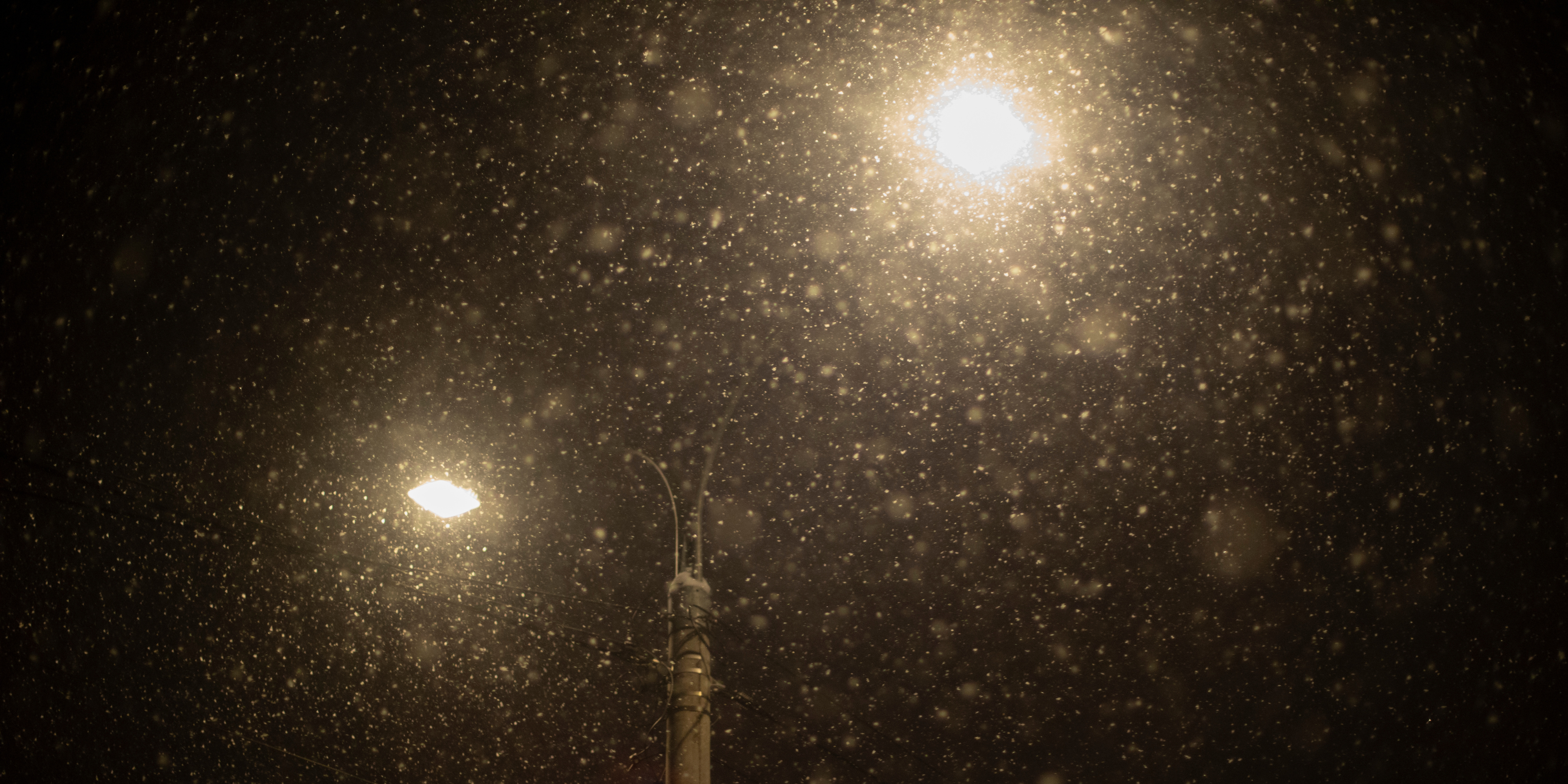 A winter night sky with snow falling across two bright lampost lights