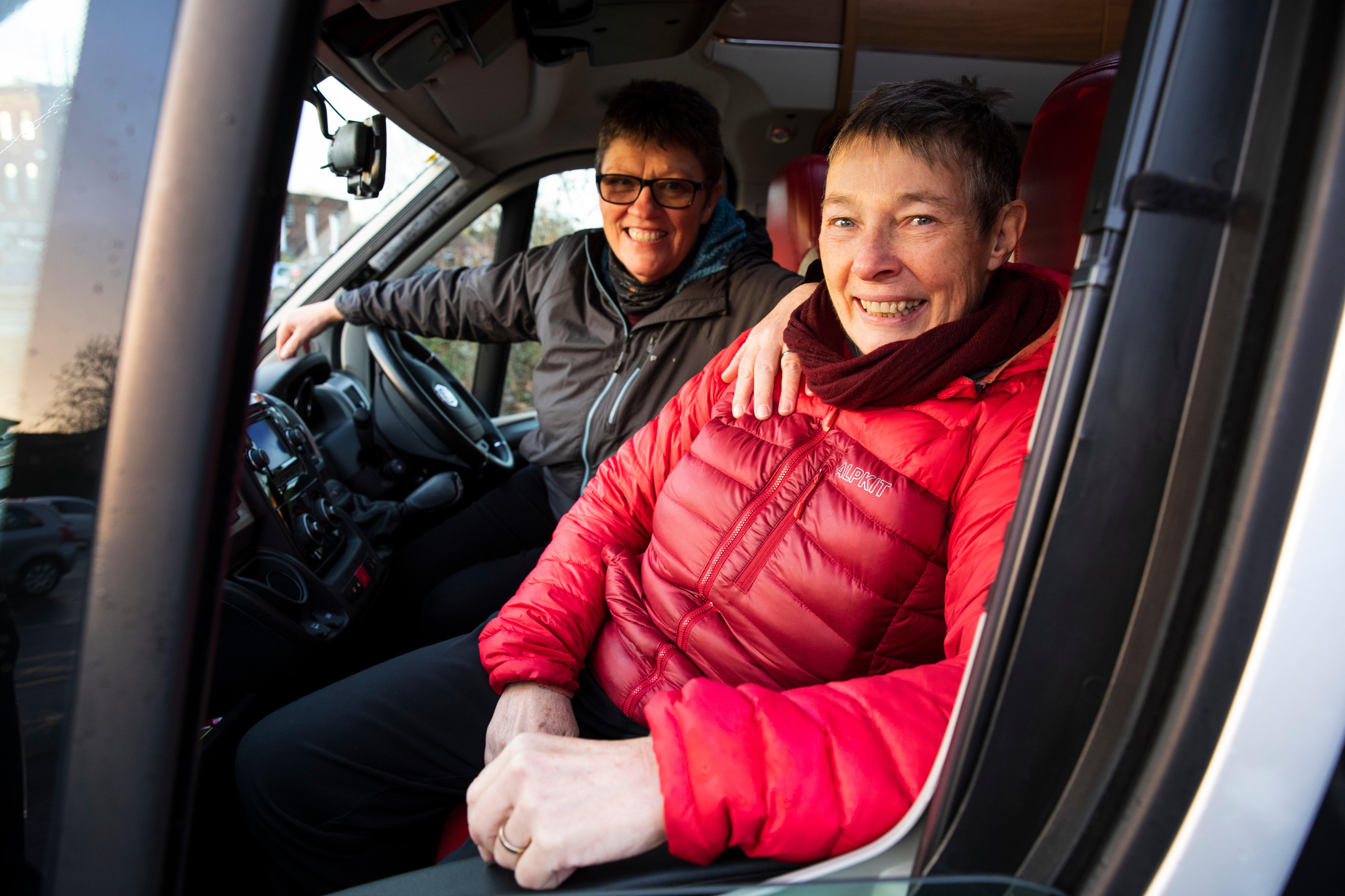A couple sits in a van, smiling at the camera