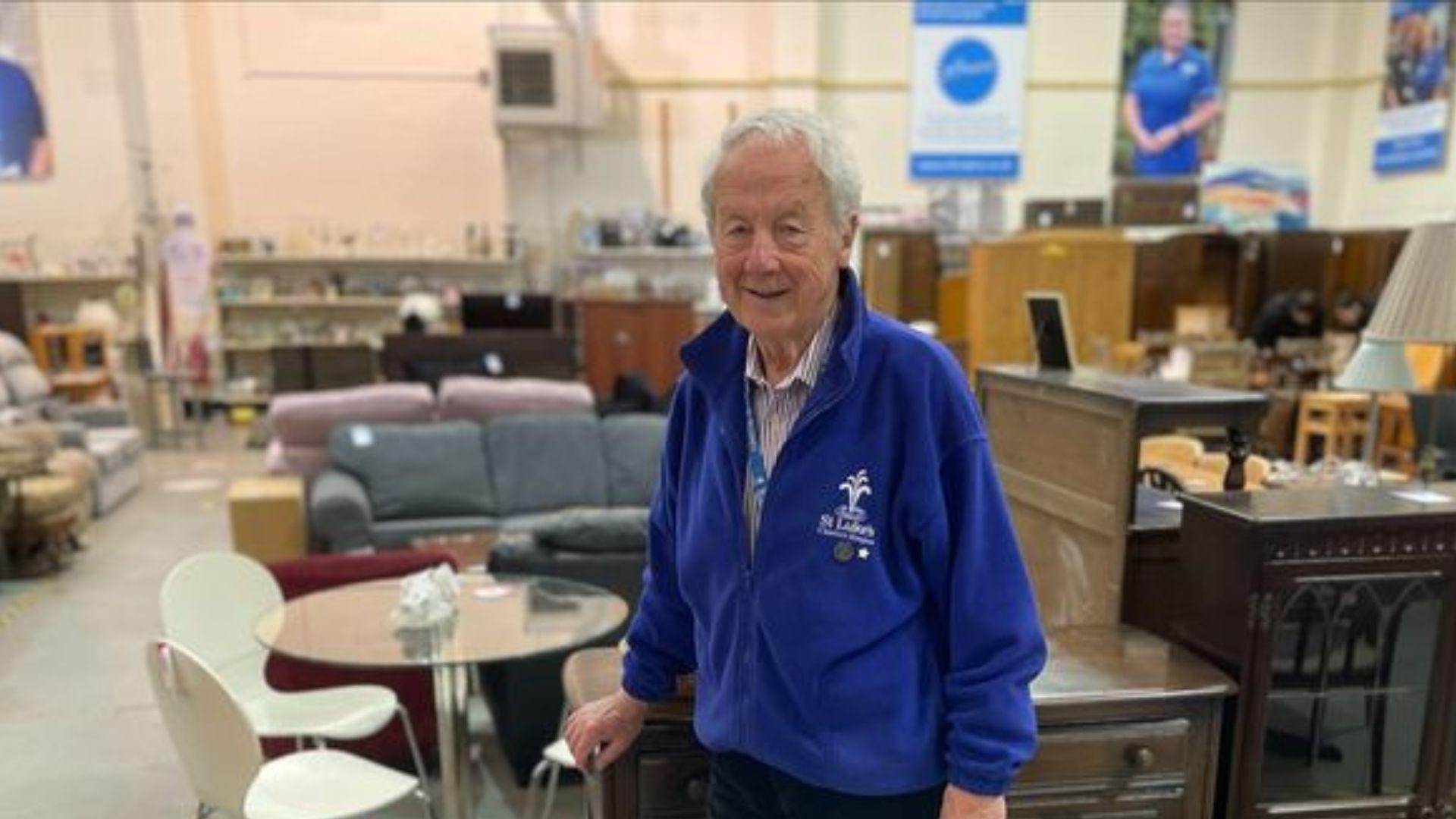 An elderly man standing in a clothing warehouse and smiling