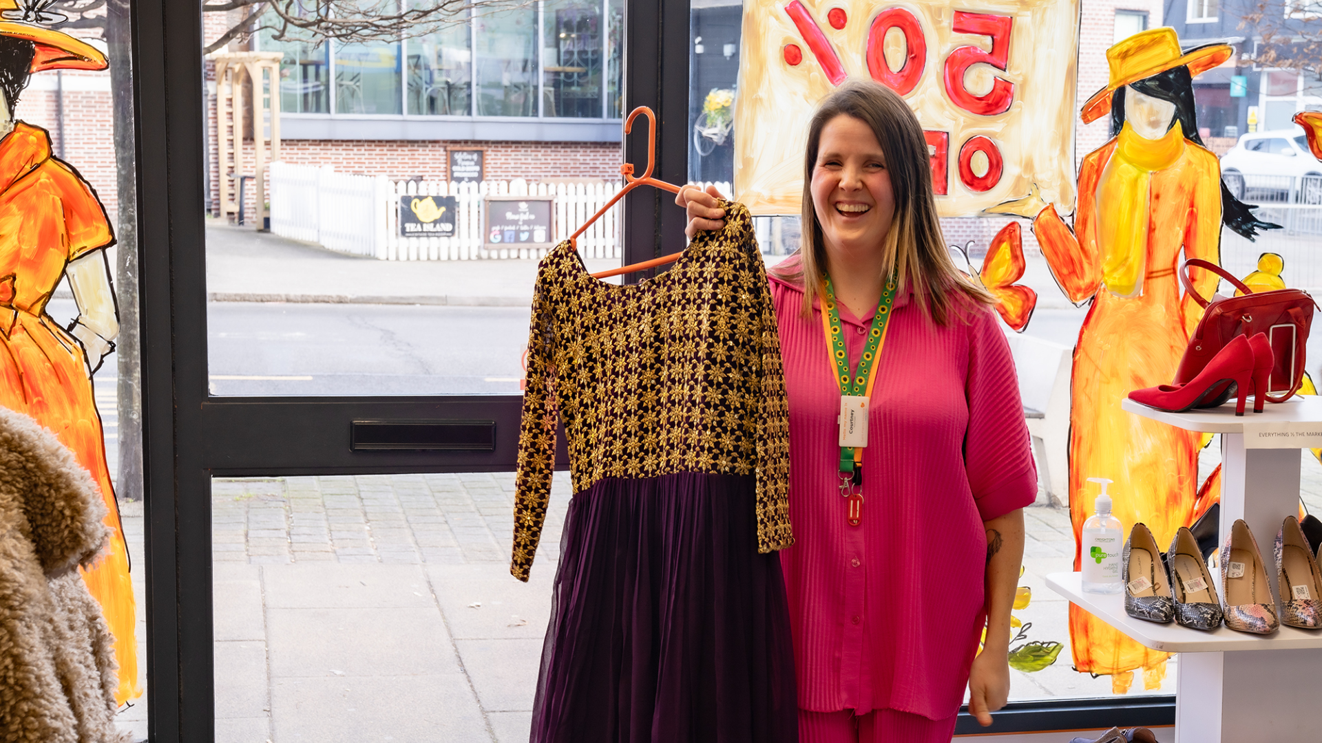 Woman standing in shop holding up dress on hanger