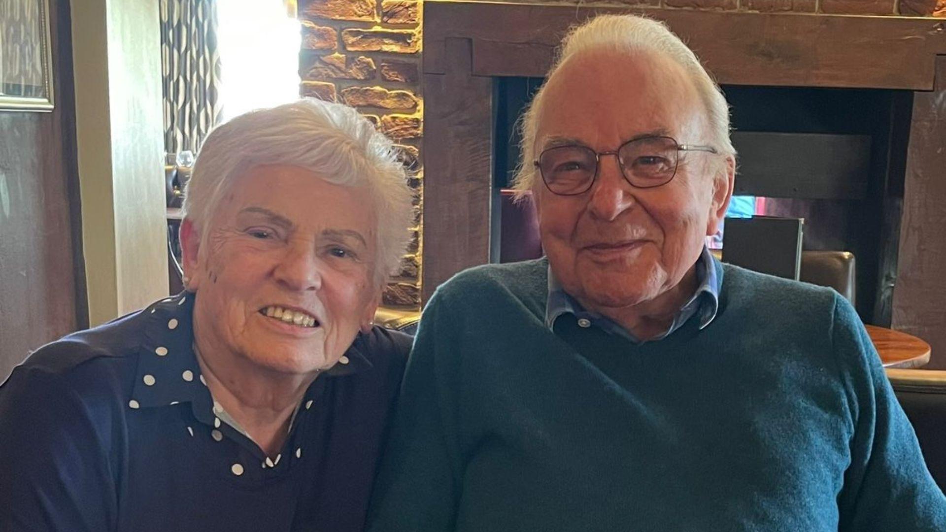 An elderly woman (left) and elderly man (right) sitting together and smiling