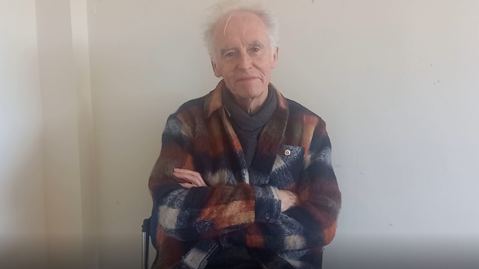 An elderly man crossing his arms and smiling at camera