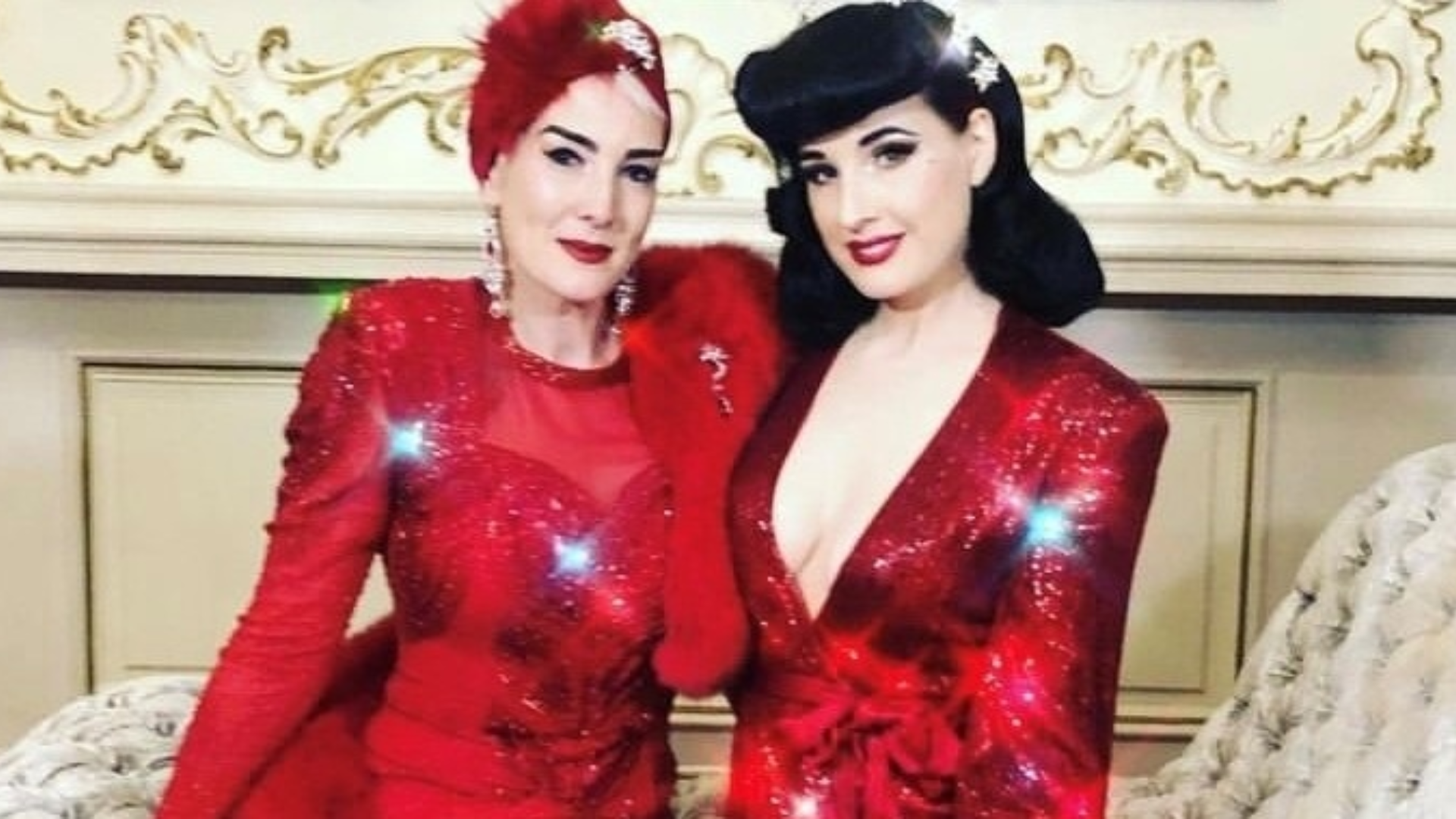 Two women wearing red dresses and hats with arms around eachother