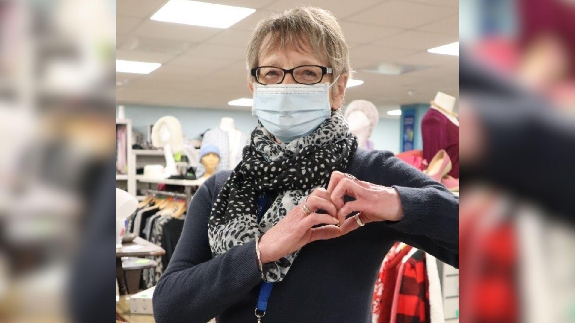 An older woman wearing a face mask and creating a heart with her hands