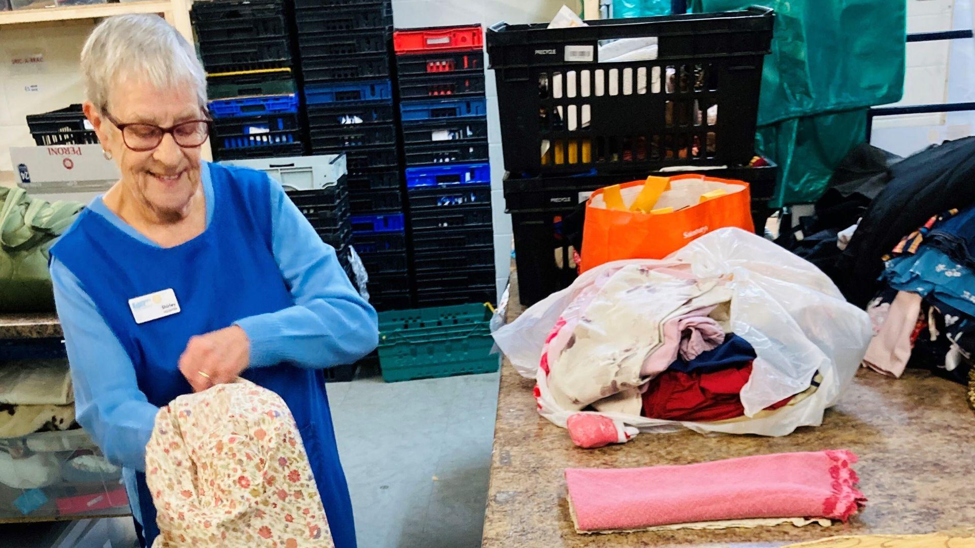 An older lady fixing clothing in a charity shop