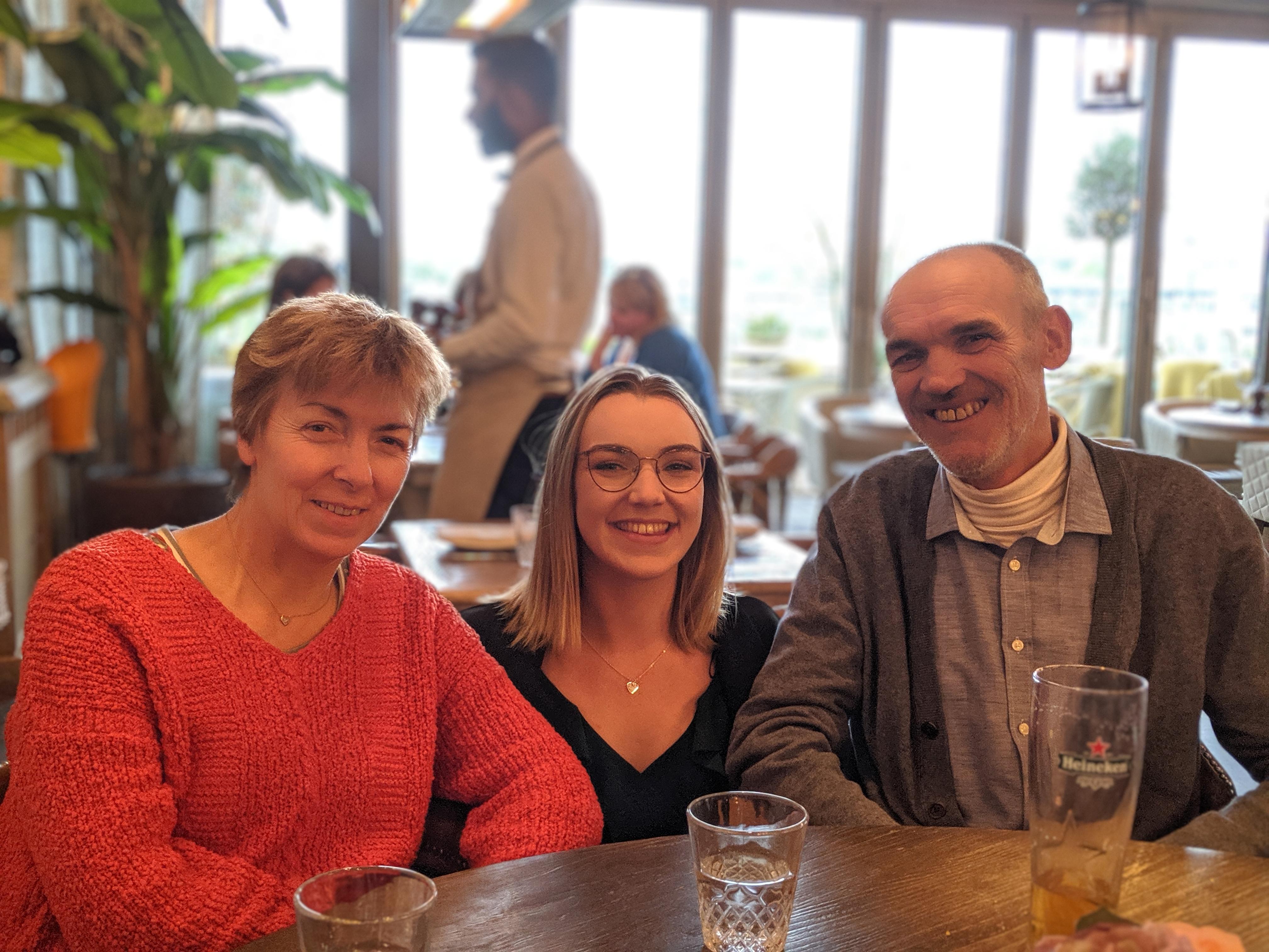 Lucy crouching in between her parents at a restaurant table