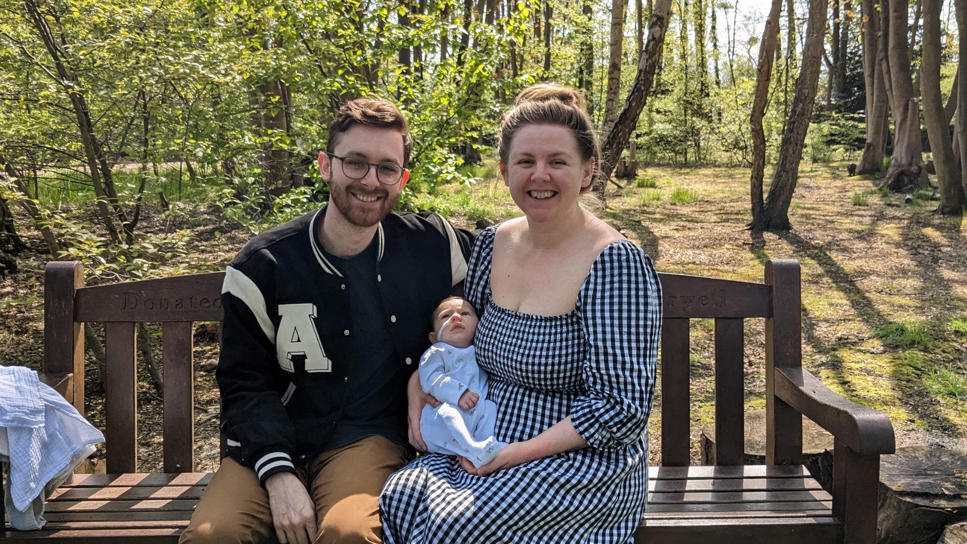A man and woman sat on a bench in a park holding their toddler