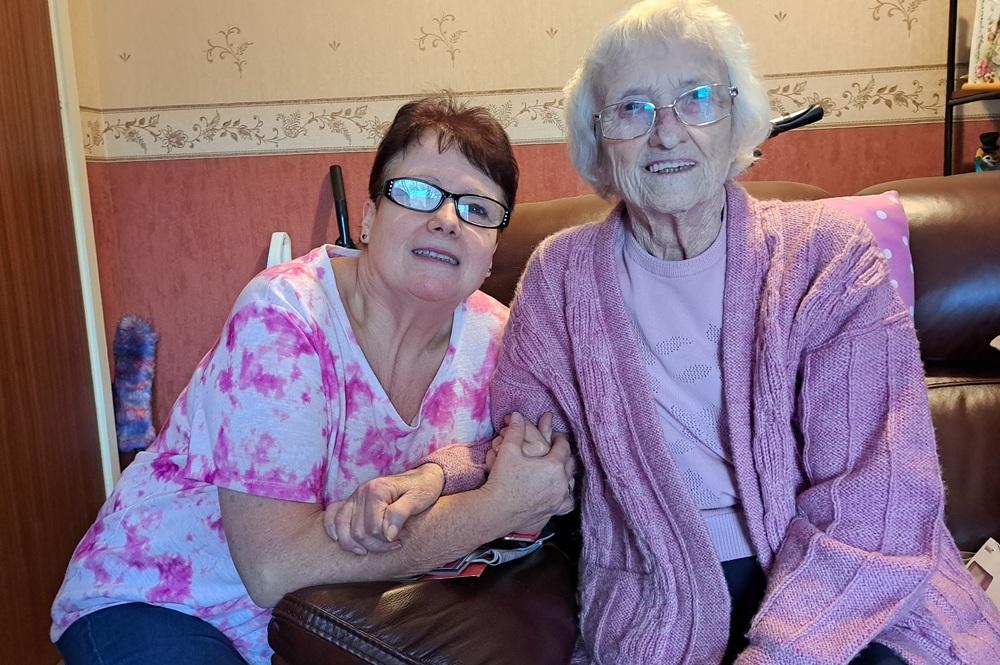 An elderly patient and daughter holding hands and sitting on an armchair