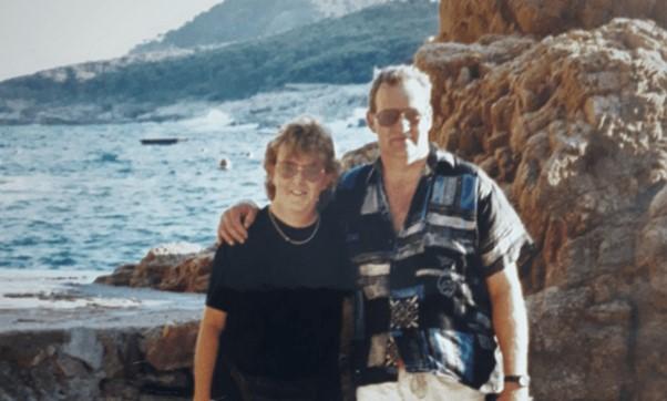 A couple standing together with the coast behind them