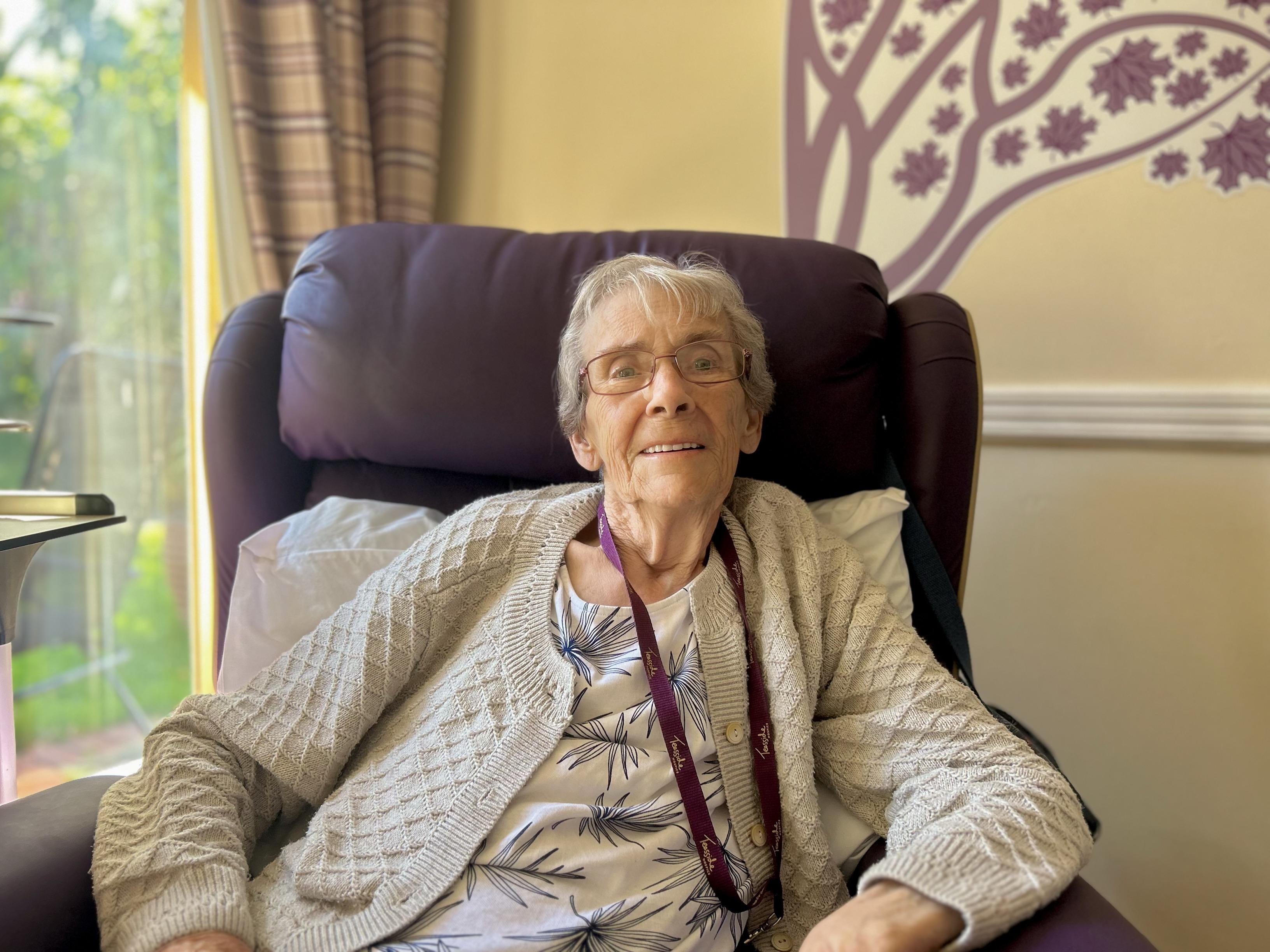 An elderly lady with short cropped hair sitting in a winged back chair