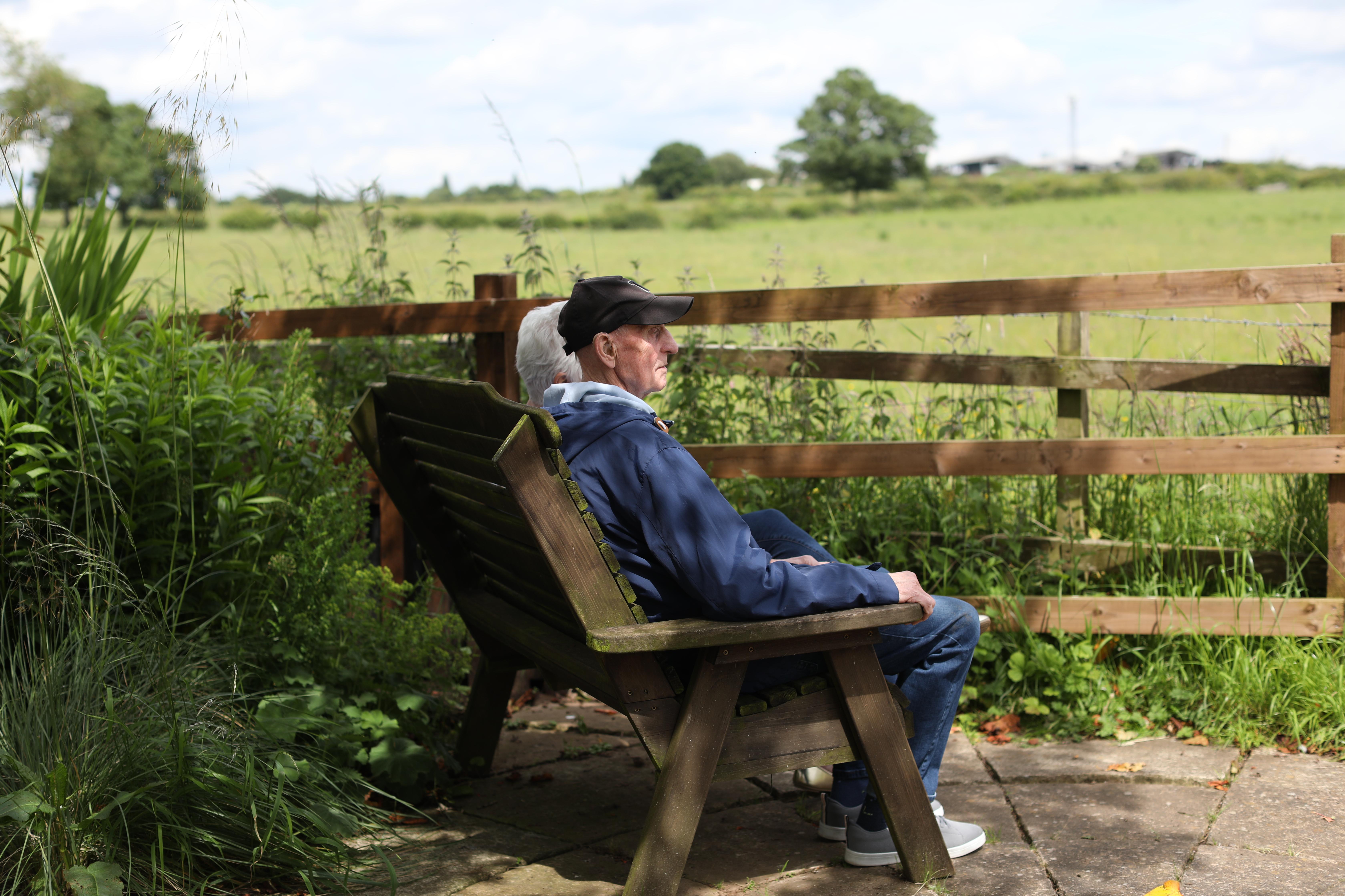 An elderly couple sat on a bench facing a view of nature