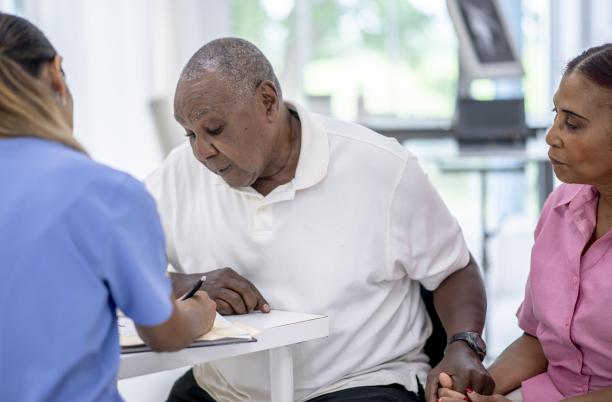 Elderly man looks at a piece of paper while holding his wife's hand