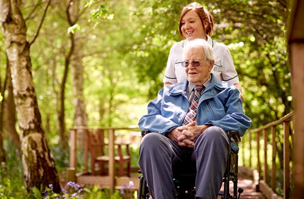 A hospice nurse with a patient in a wheelchair admiring the hospice gardens