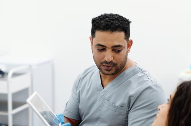 Male nurse wearing scrubs showing a tablet screen to female patient