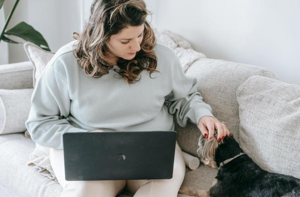 woman sitting on a couch with a pet dog and a laptop