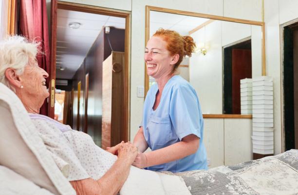 Laughing nurse sits at the bed of an elderly woman