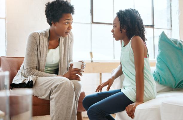 A mother holding a hot drink and sitting in conversation with a young girl