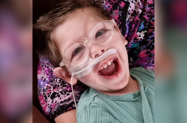 A toddler wearing glasses laughing at the camera