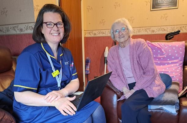 A elderly patient sat on an armchair next to a palliative care nurse