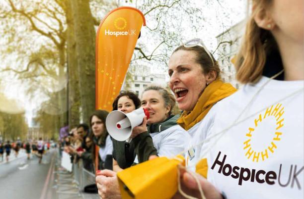 A crowd of people along a fence cheering, with a woman in the middle cheering into a loudhailer