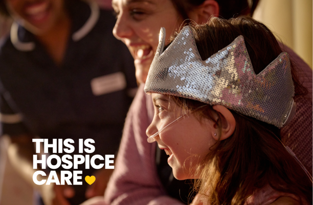 A girl in a crown wearing an oxygen tube is laughing with her mum and a nurse. The text in the corner reads 'This is hospice care'.