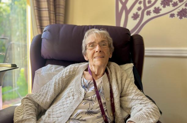 An elderly lady with short cropped hair sitting in a winged back chair