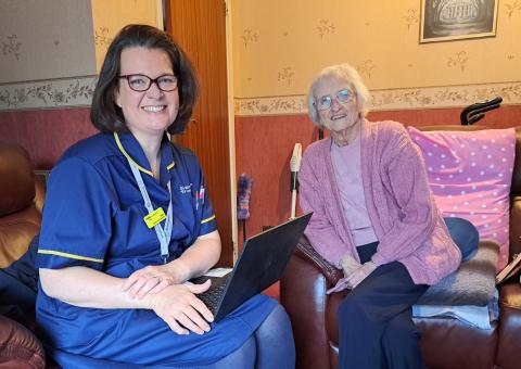 A elderly patient sat on an armchair next to a palliative care nurse