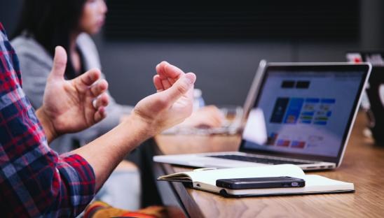 A stock photo showing someone talking at a meeting with a PC in front of them