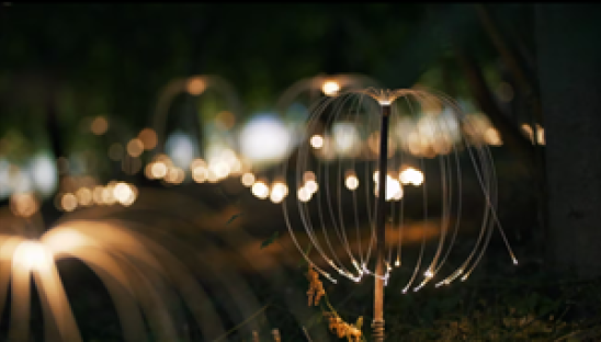 A small, outdoor light installation in the shape of a firefly during the night