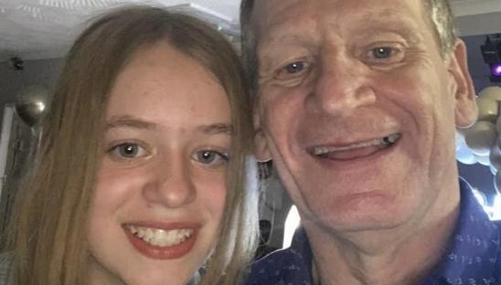 A teenager with long, brunette hair taking a selfie with her father